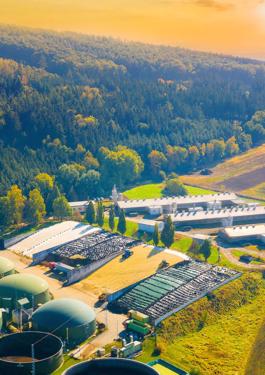 Biogas plant and farm in green fields against sunset
